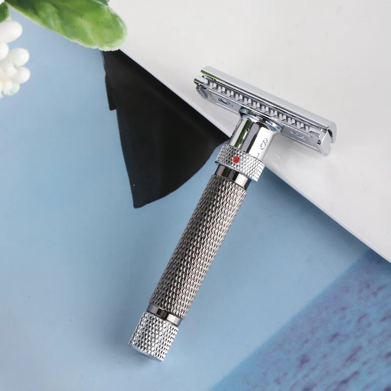 The Kelvedge safety razor resting at an angle against a white ledge on a pale blue surface, showing the guard bar and single blade slot of the chrome head